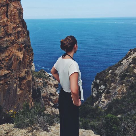 Frau im Sommer steht auf einer Klippe am Meer