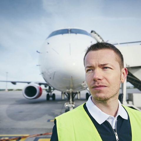 Flughafenmitarbeiter in Warnweste steht vor Flugzeug