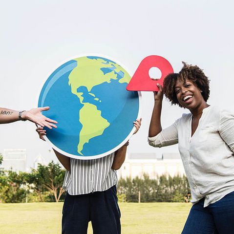 Internationale Menschen zeigen mit Pinnnadel auf Weltkugel und lächeln