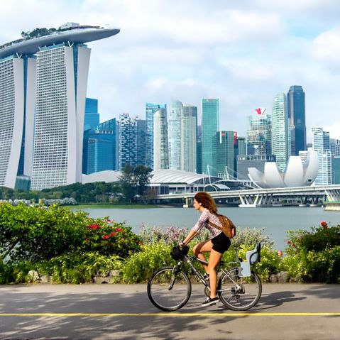 Die Skyline von Singapur vor der eine Frau mit einem Fahrrad fährt