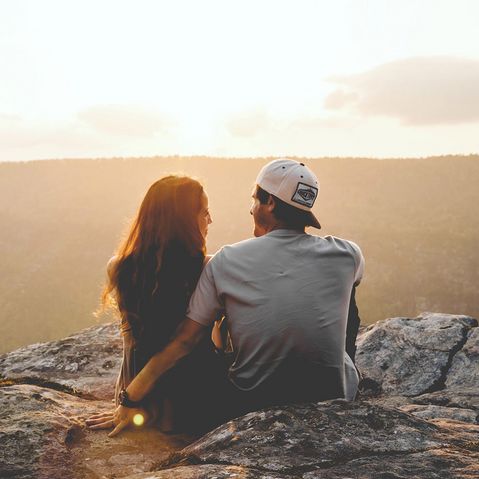 Junges Paar auf Felsen sitzend genießt Sonnenuntergang