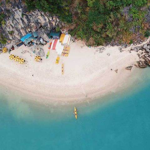 Ein Strand in Vietnam von der Dronenperspektive mit Kayas auf dem blauen Meer und grünen Bergen